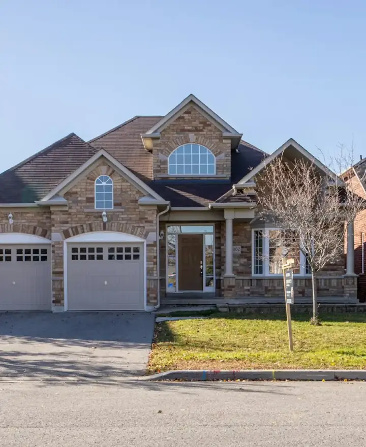 Stone two-storey home with a double garage and a maple out front